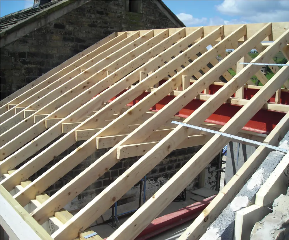 New timber roof structure under construction, rafters and firrings set out over a stone wall plate