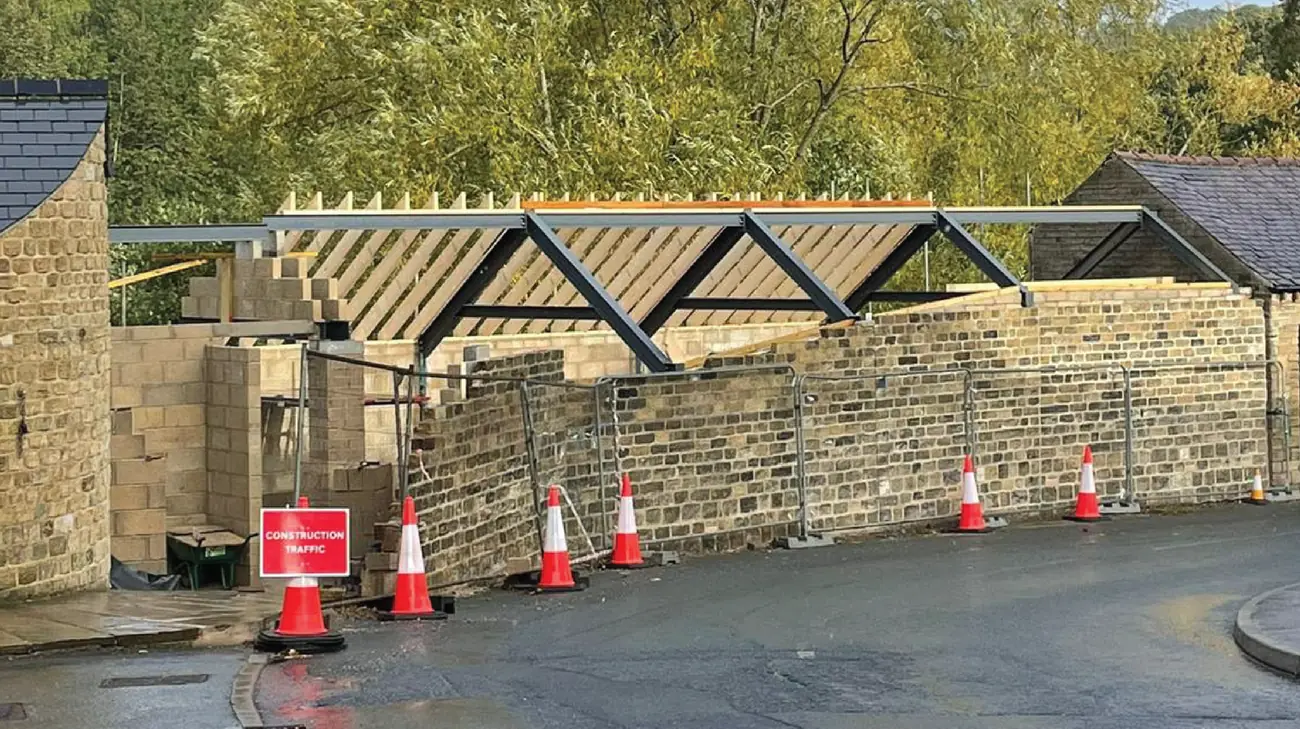 Steelwork and trusses in place on site behind hoarding and traffic management
