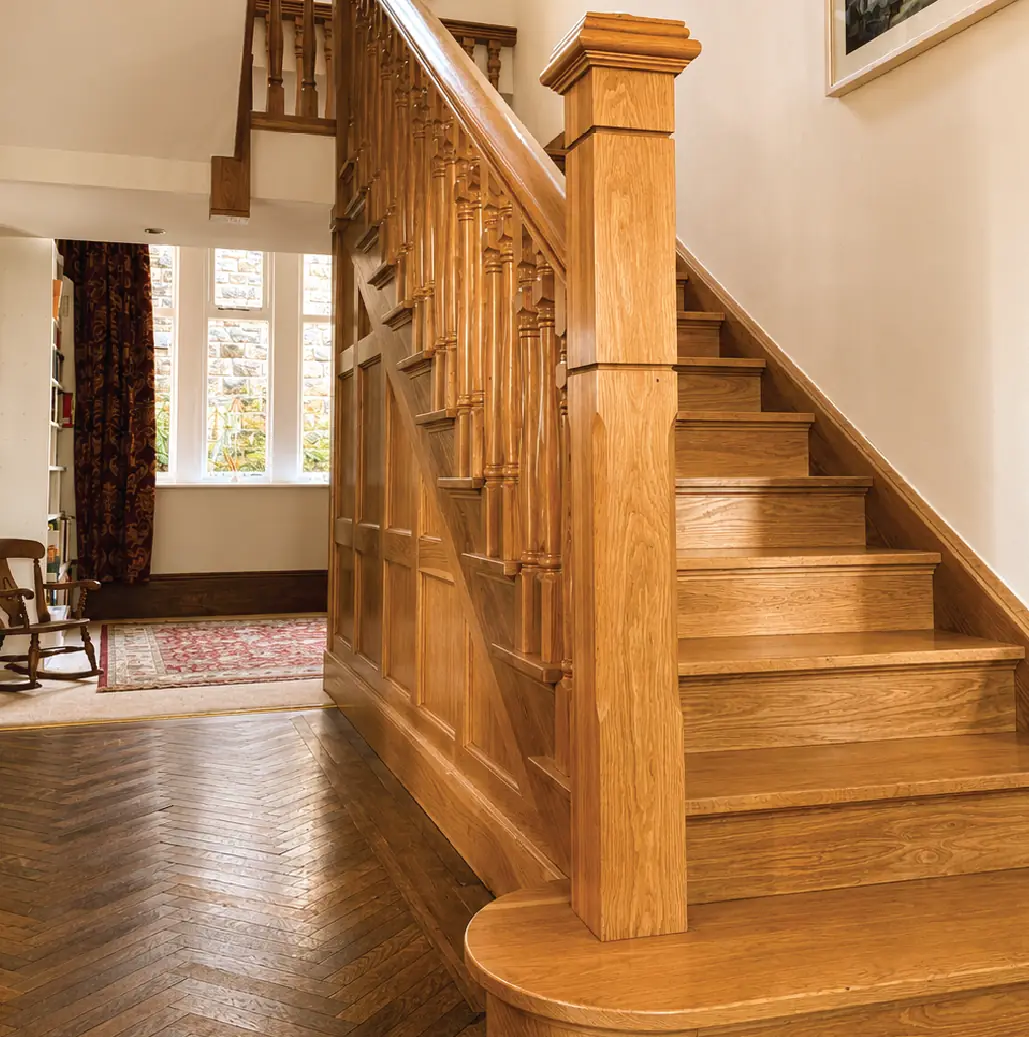 Panelled oak staircase with a curtail step above a herringbone parquet floor