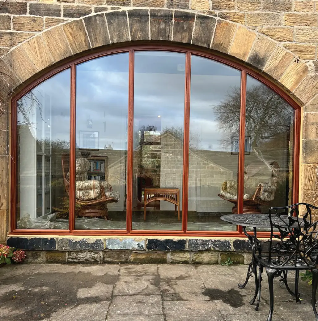 Arched hardwood window to a stone barn, overlooking a flagged terrace